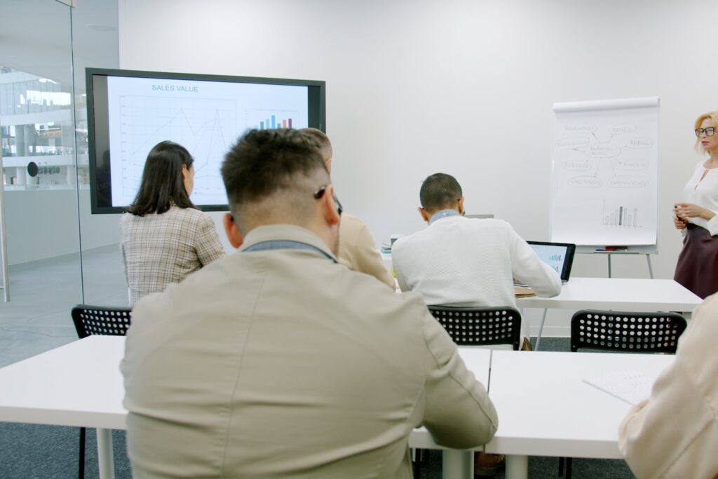 Mature businesswoman making presentation in office room for employees talking pointing at information of board. People and modern business concept.